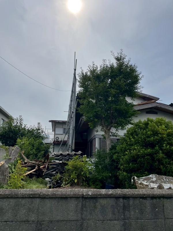 解体前の住宅。塀の向こうに建物と庭木が見える