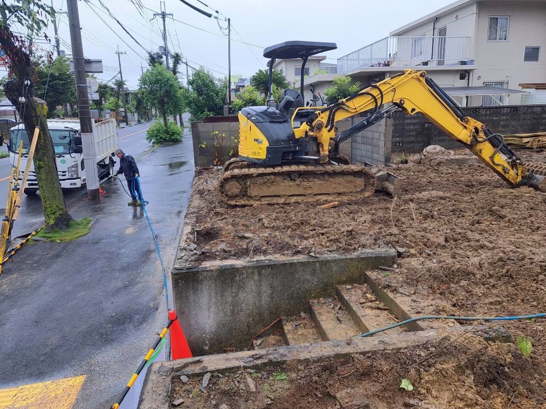 整地中の現場で重機が作業し、作業員が散水している